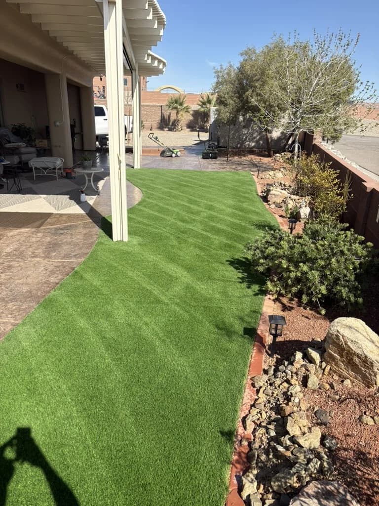 Restored artificial turf side yard in a Mesquite Nevada backyard, upright vibrant fibers, stone patio and desert landscaping in the background